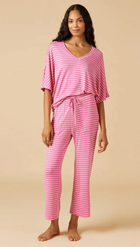 Model wearing a pink and white striped lounge set featuring a relaxed V-neck top with elbow-length sleeves and matching drawstring pants against a neutral studio backdrop.