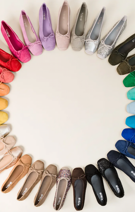 A full spectrum of suede ballet flats arranged in a circle on a light background, showing dozens of colors from red and pink to blue, green, gray, and black.