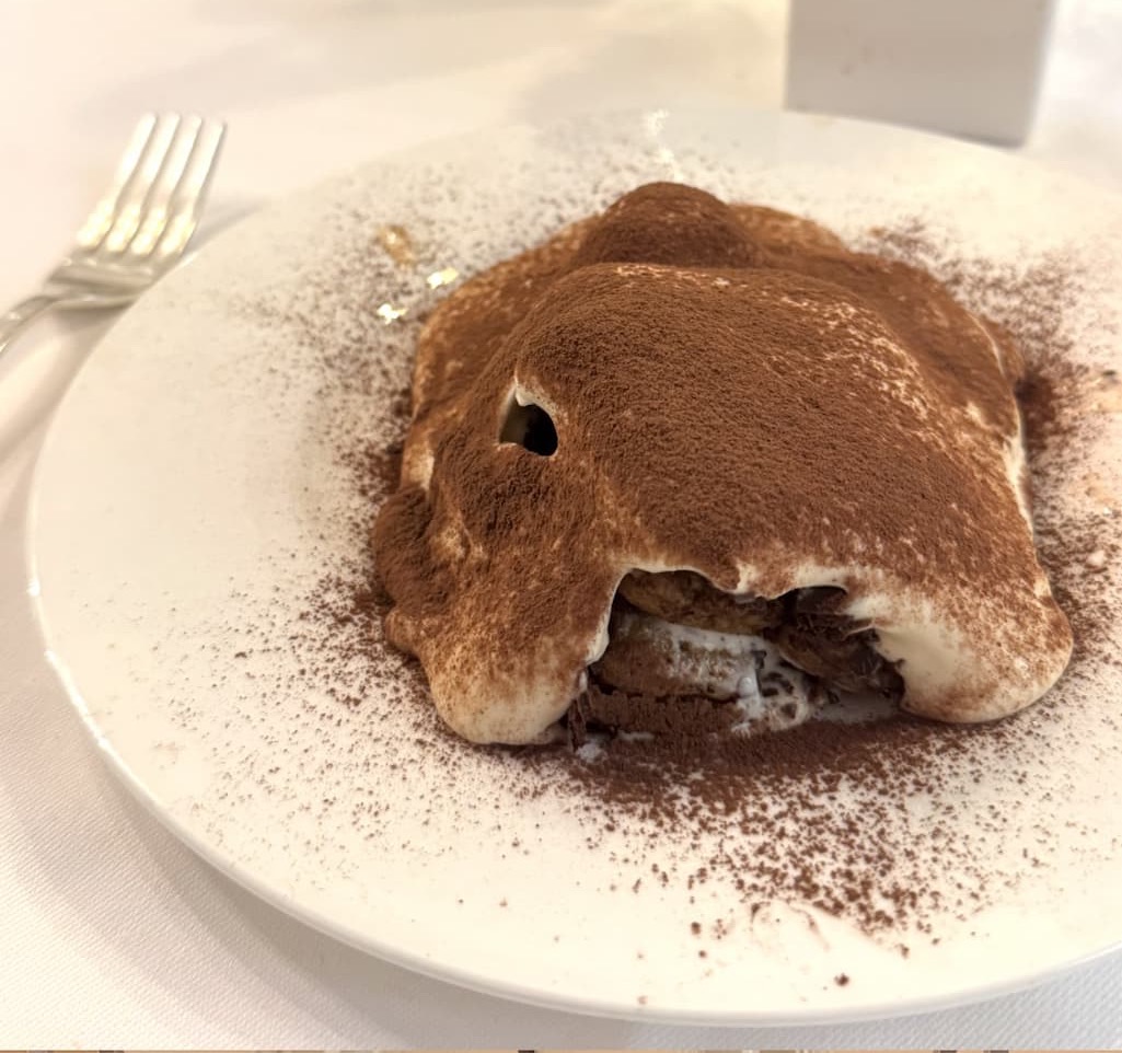 Partially eaten tiramisu on a white plate, dusted with cocoa powder, revealing layers of mascarpone cream and soaked ladyfingers inside.