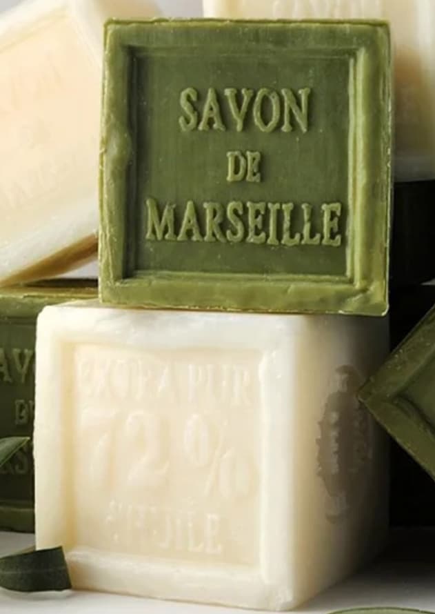 Stacked bars of traditional Marseille soap, one olive green and one creamy white, with embossed lettering highlighting their origin and olive oil content.