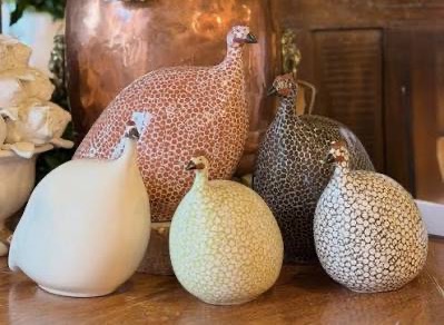 Handcrafted ceramic guinea fowl sculptures displayed beside white hydrangeas in a warm, inviting home décor setting. Fearrington Village.
