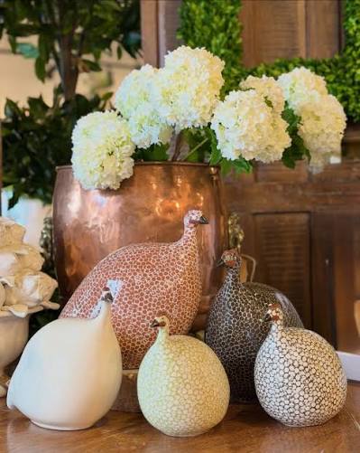 Decorative ceramic guinea fowl sculptures in neutral speckled finishes arranged with white hydrangeas in a copper vase. Fearrington Village.