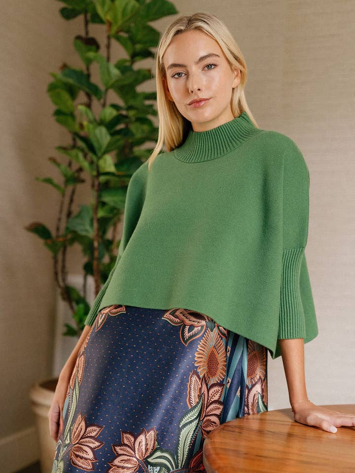 A woman models a cropped green mock-neck sweater with three-quarter sleeves, paired with a navy floral-print skirt. Fearrington Village.