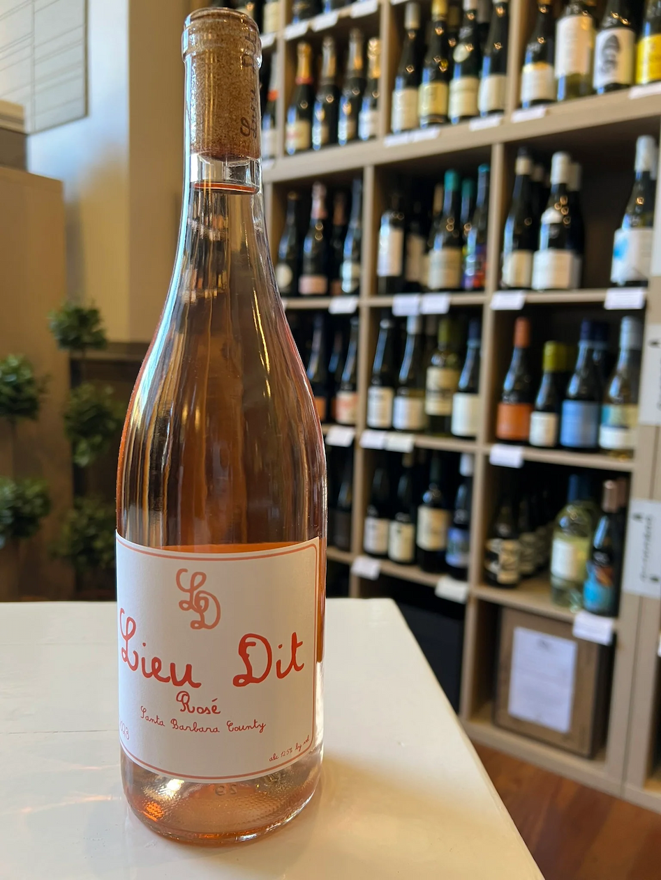 Bottle of Lieu Dit Rosé displayed on a counter in front of shelves filled with curated wines inside a wine shop. Fearrington Village.