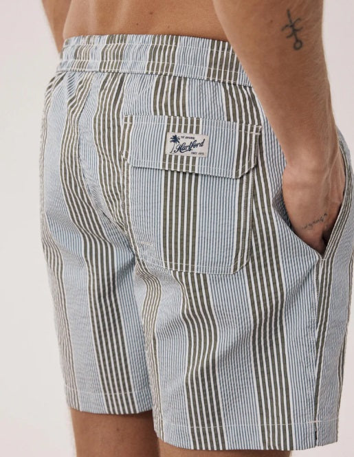 Men’s striped swim shorts in muted olive, blue, and white with an elastic waistband, back flap pocket, and relaxed tailored fit.