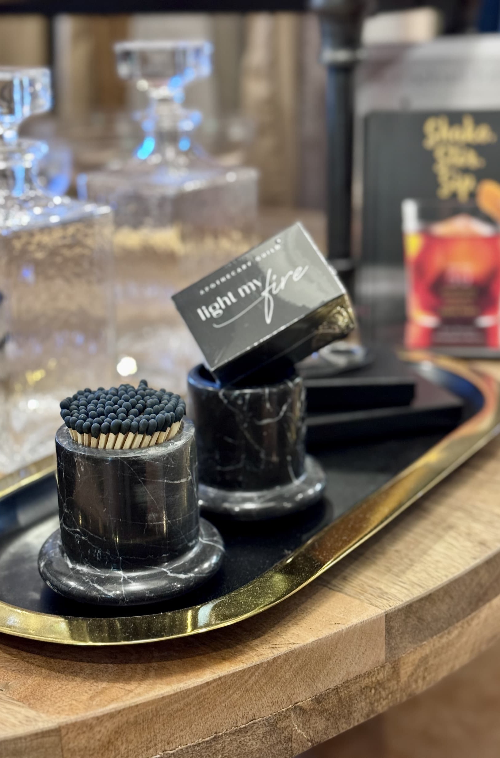 Black marble match holder and boxed matches displayed on a brass tray alongside crystal barware, creating a sophisticated bar cart vignette. Fearrington Village.