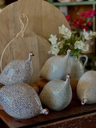 Collection of handcrafted ceramic guinea fowl sculptures displayed on a rustic table with wooden serving boards and fresh flowers. Fearrington Village.