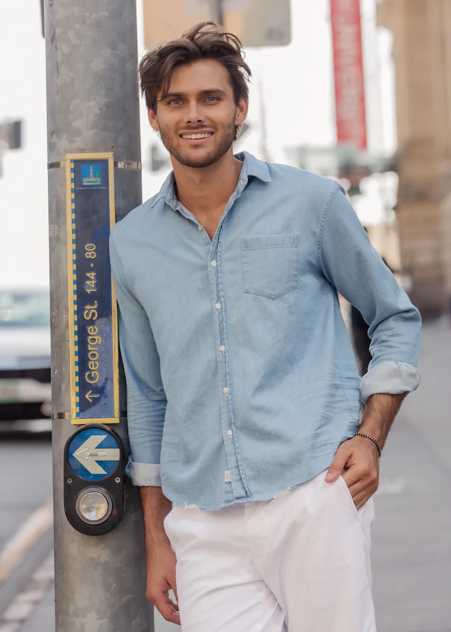 Man wearing a light blue button-down shirt and white pants, standing on a city sidewalk. Fearrington Village.