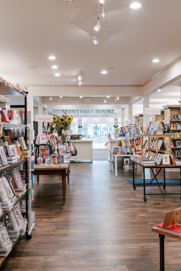 Bright interior of McIntyre's Books featuring tables of new releases, shelves of books, and a welcoming open layout with the bookstore's signature sign in the background. Fearrington Village.