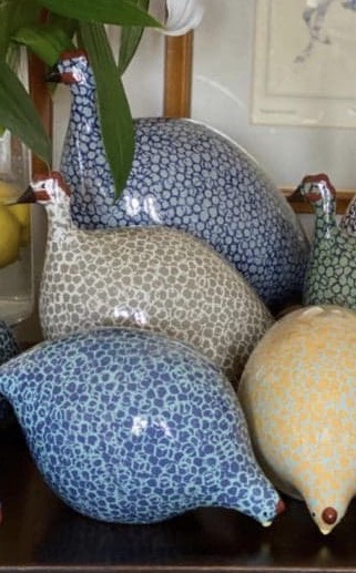 Colorful ceramic guinea fowl sculptures in assorted speckled patterns displayed with fresh lilies. Fearrington Village.