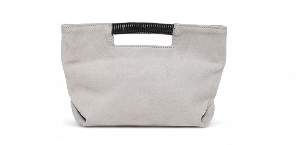Soft gray suede clutch with a relaxed rectangular silhouette, featuring a cutout top handle wrapped in black detailing and a minimalist, slightly slouched design.