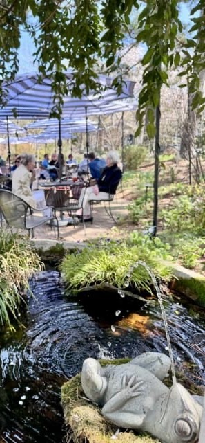 Shaded garden patio with guests dining beside a fountain and lush greenery. Fearrington Village.