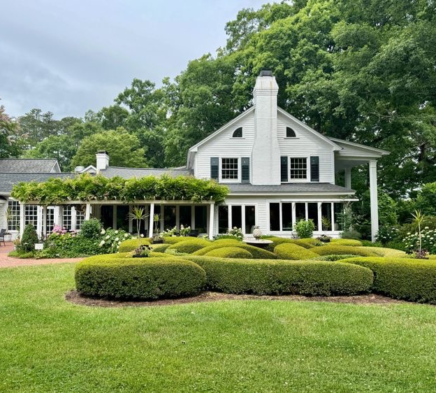White farmhouse surrounded by manicured gardens, sculpted boxwoods, and a vine-covered pergola. Fearrington Village.