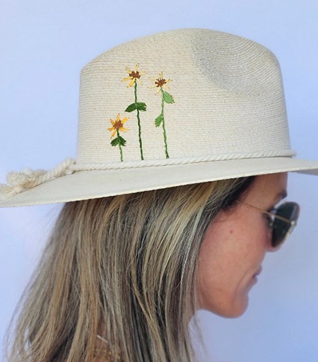 Side profile of a woman wearing a natural straw hat embroidered with delicate yellow wildflowers, paired with sunglasses and a sleeveless white top. Fearrington Village.