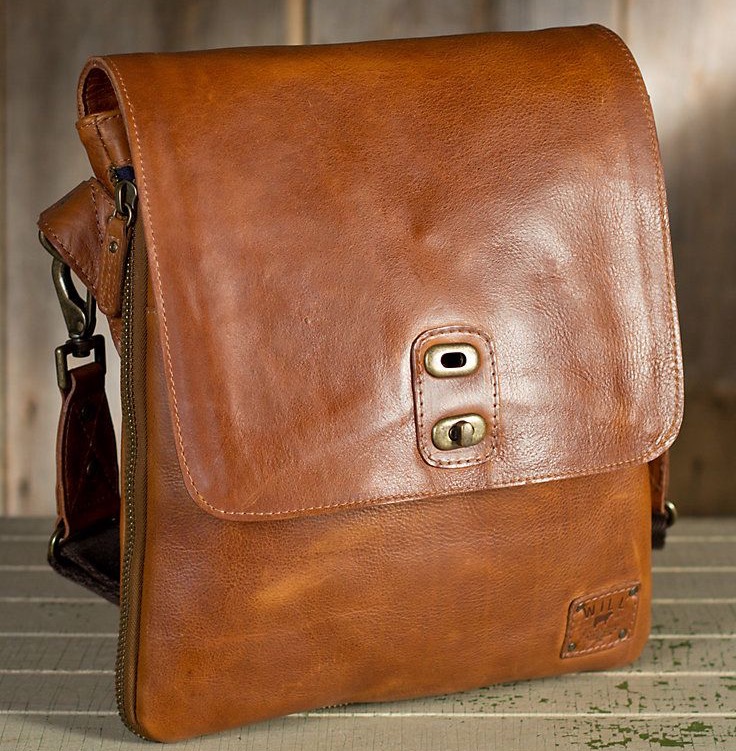 Brown leather crossbody bag with a smooth, worn-in finish and a flap closure featuring a brass turn-lock detail. Includes a shoulder strap and subtle stitching, set against a rustic wood backdrop.