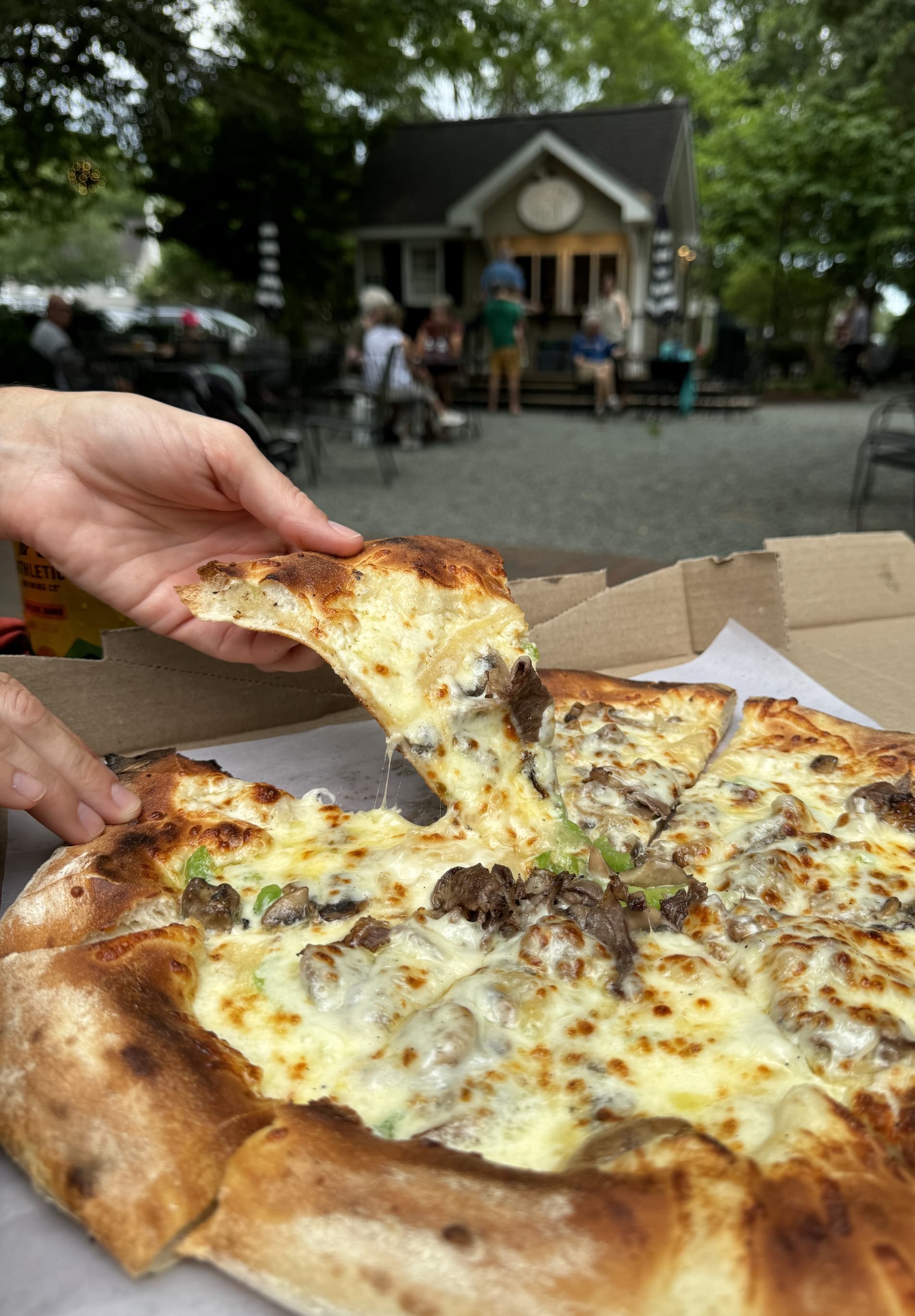 Cheesy mushroom and green pepper pizza with a slice being lifted from the pie at an outdoor table. Fearrington Village.