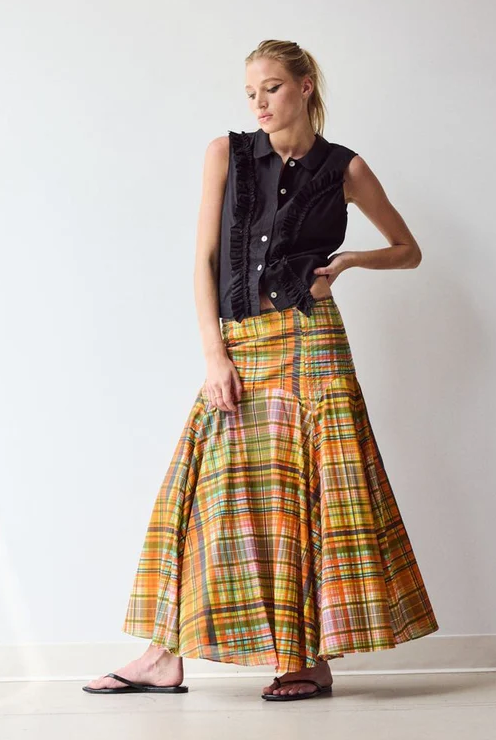 Woman wearing a black ruffle-trim sleeveless blouse with a flowing orange plaid maxi skirt and black sandals, Fearrington Village.