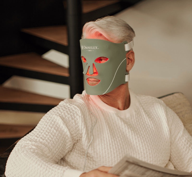 Man wearing a light therapy face mask while sitting and reading a newspaper.