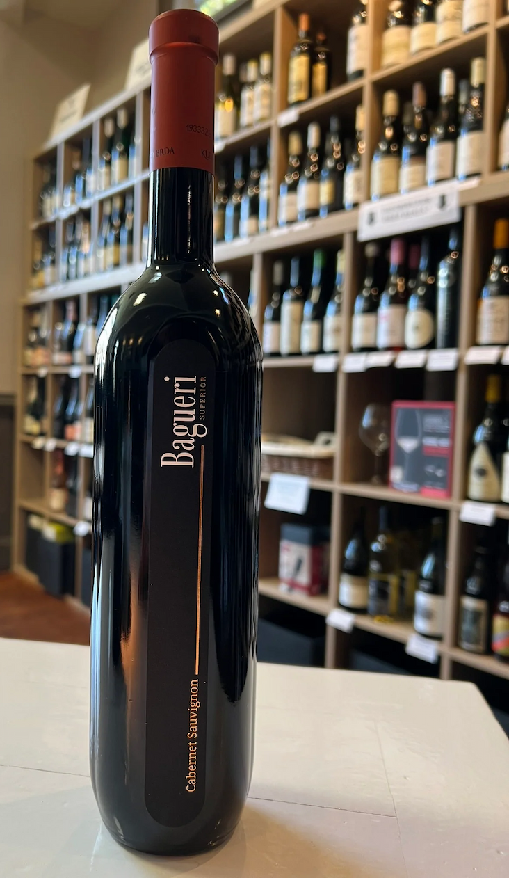 A bottle of Bàgeri Cabernet Sauvignon stands on a counter in a wine shop, with shelves of wine bottles softly blurred in the background.