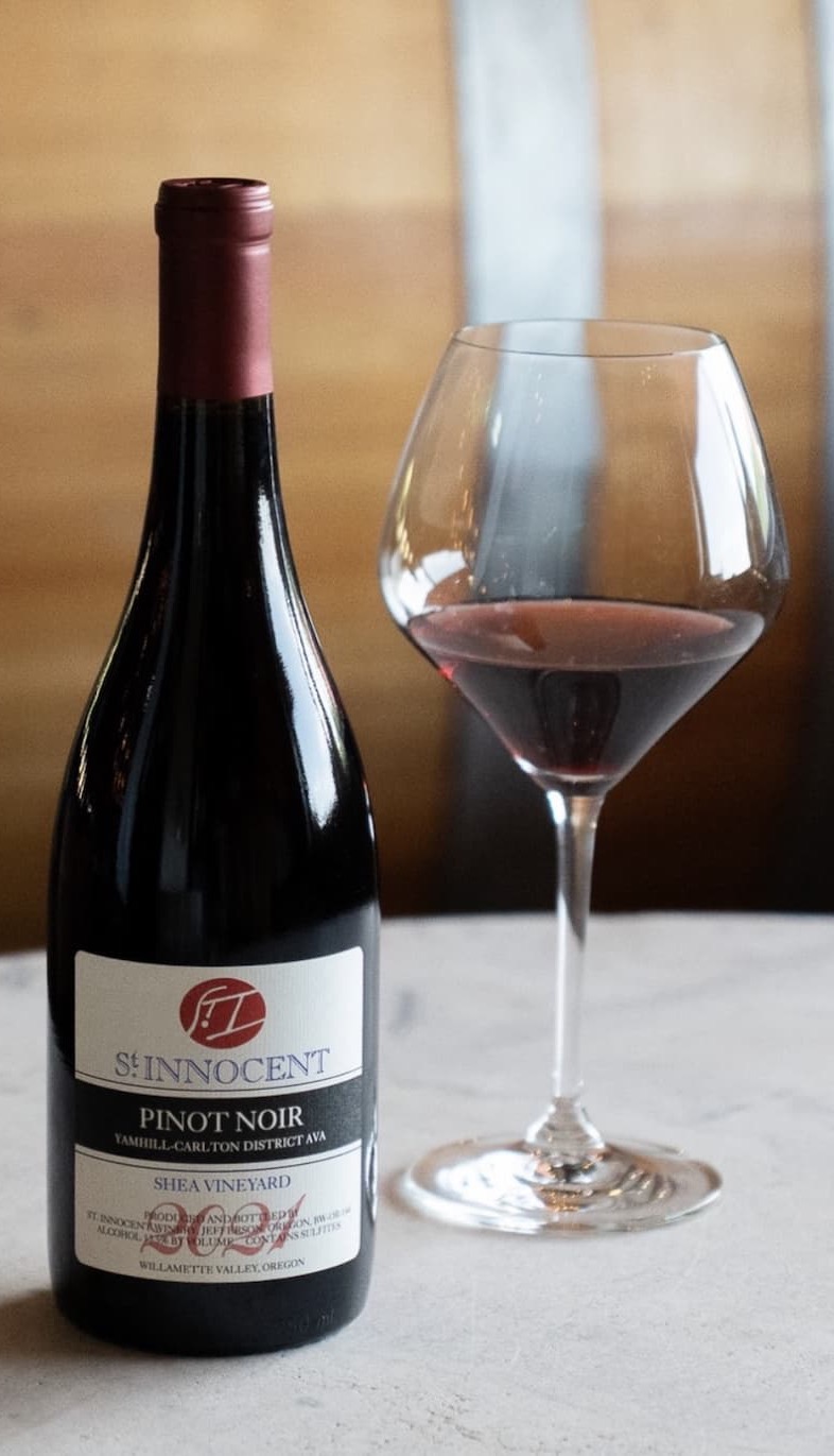 Bottle of St. Innocent Pinot Noir beside a wine glass partially filled with red wine on a tabletop.