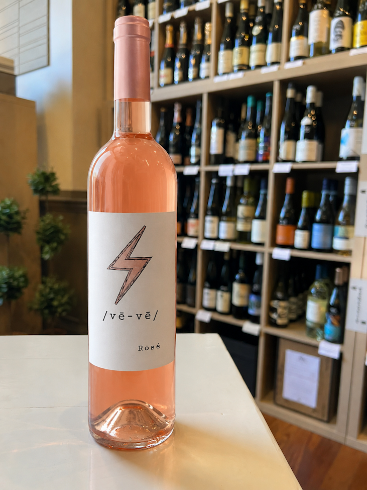 Bottle of /vē-vē/ Rosé displayed in front of a curated wall of wines. Fearrington Village.
