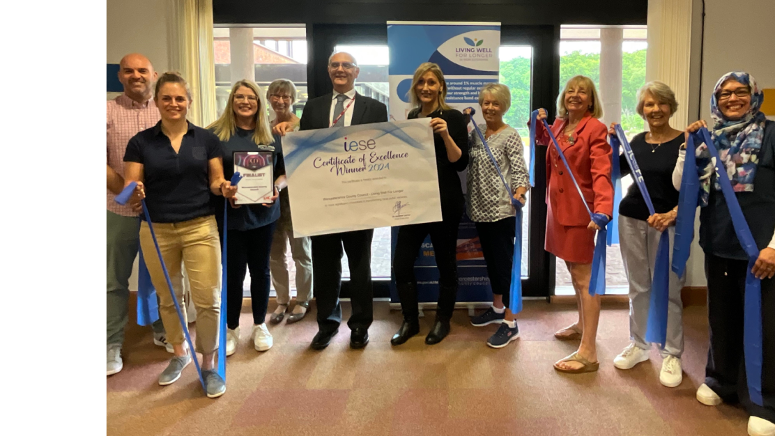 The Corn Dollies WI with Sophie Pryce, Councillor David Ross and Lisa McNally, holding resistance bands and a programme award