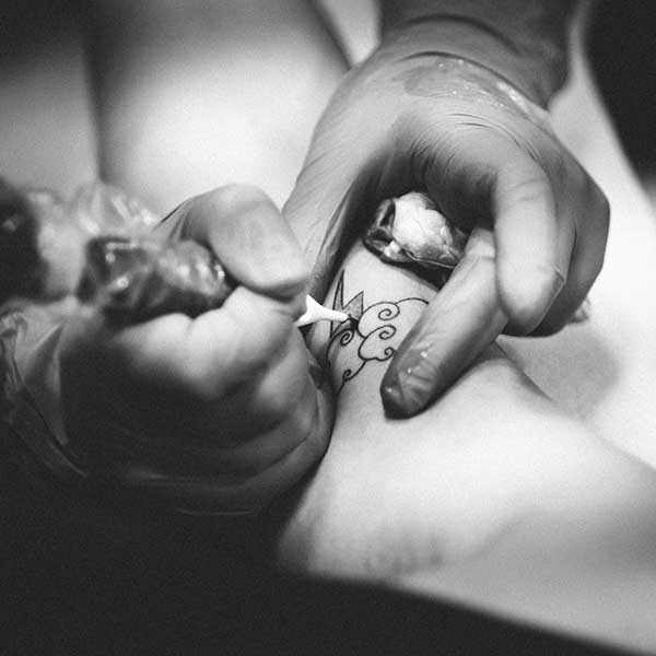 A tattoo artist working on a small tattoo. Photo by Maixent Viau on Unsplash.