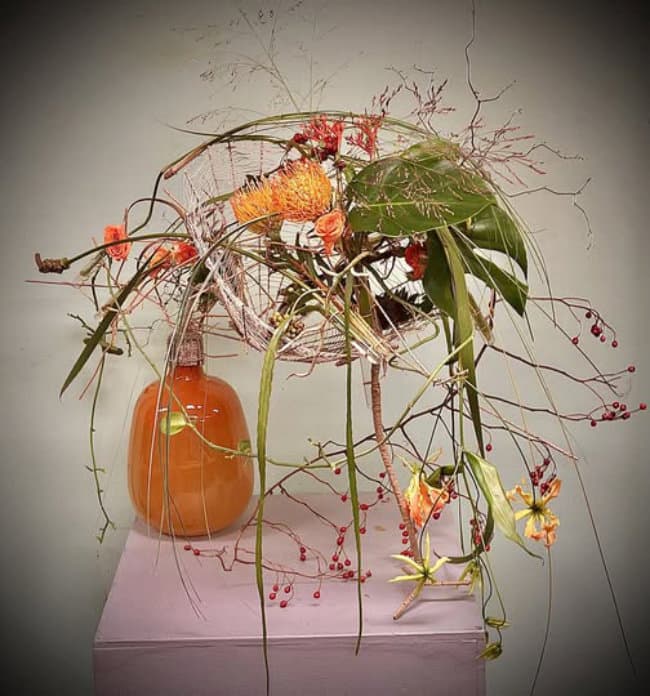 an image of a vase with flowers and leaves on a table