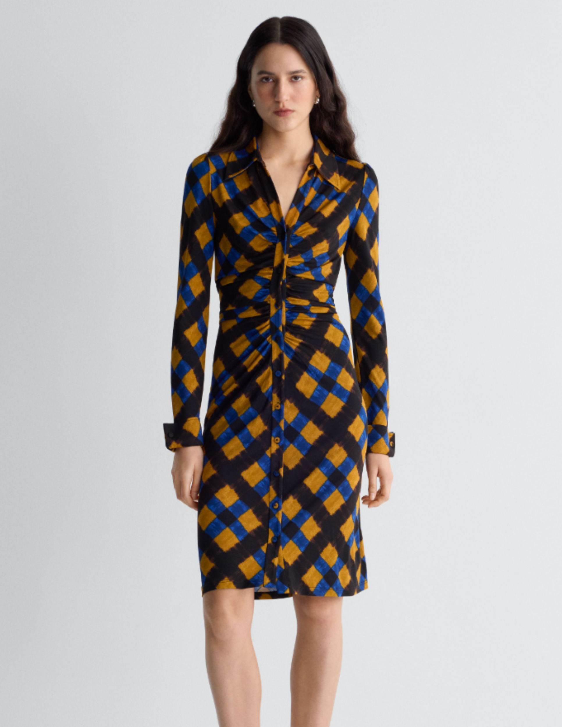 Model wearing a long-sleeve shirt dress in a blue, ochre, and black geometric print with front ruching and a button-front silhouette.