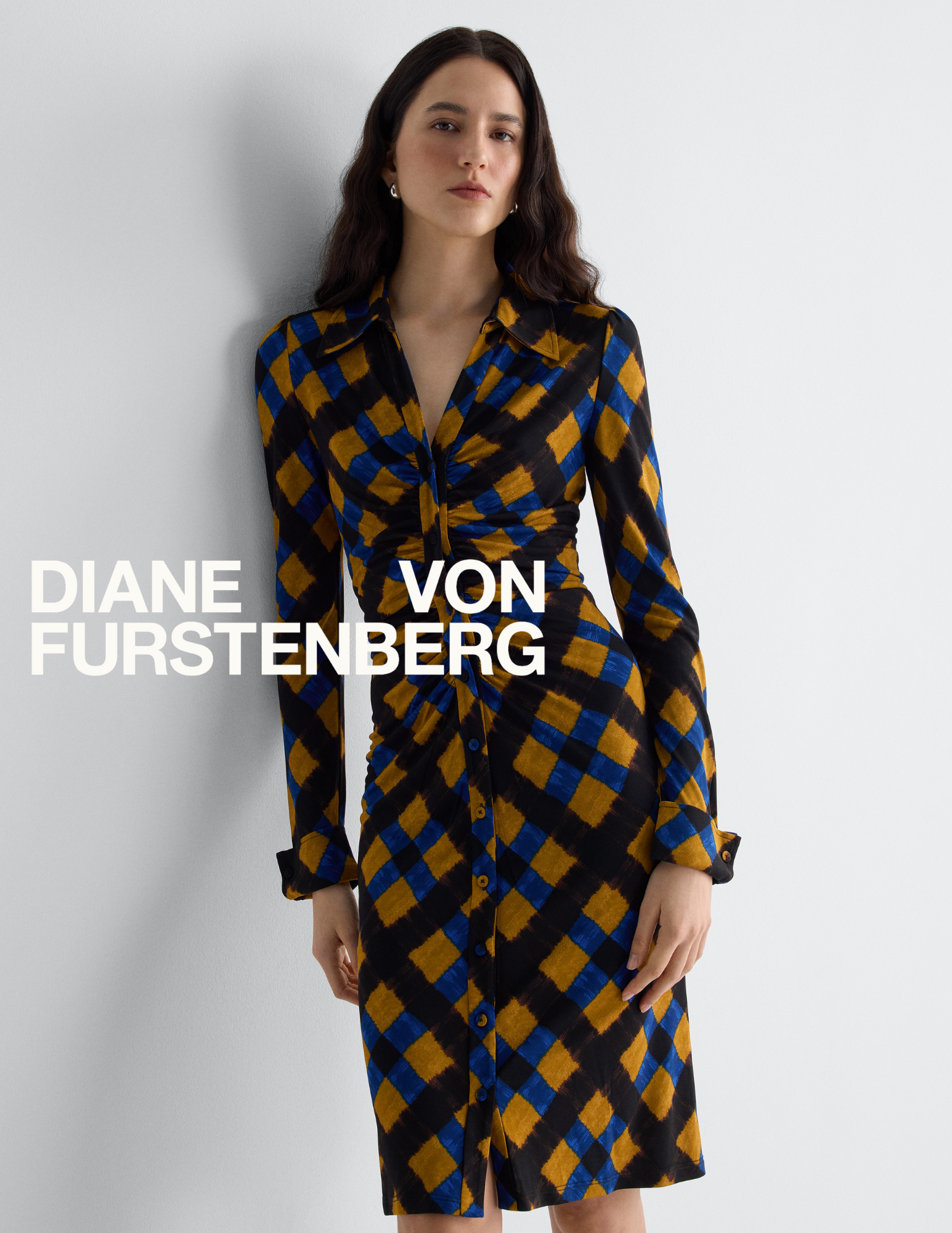 Model wearing a blue, ochre, and black geometric print ruched shirt dress with the Diane von Furstenberg logo overlay.