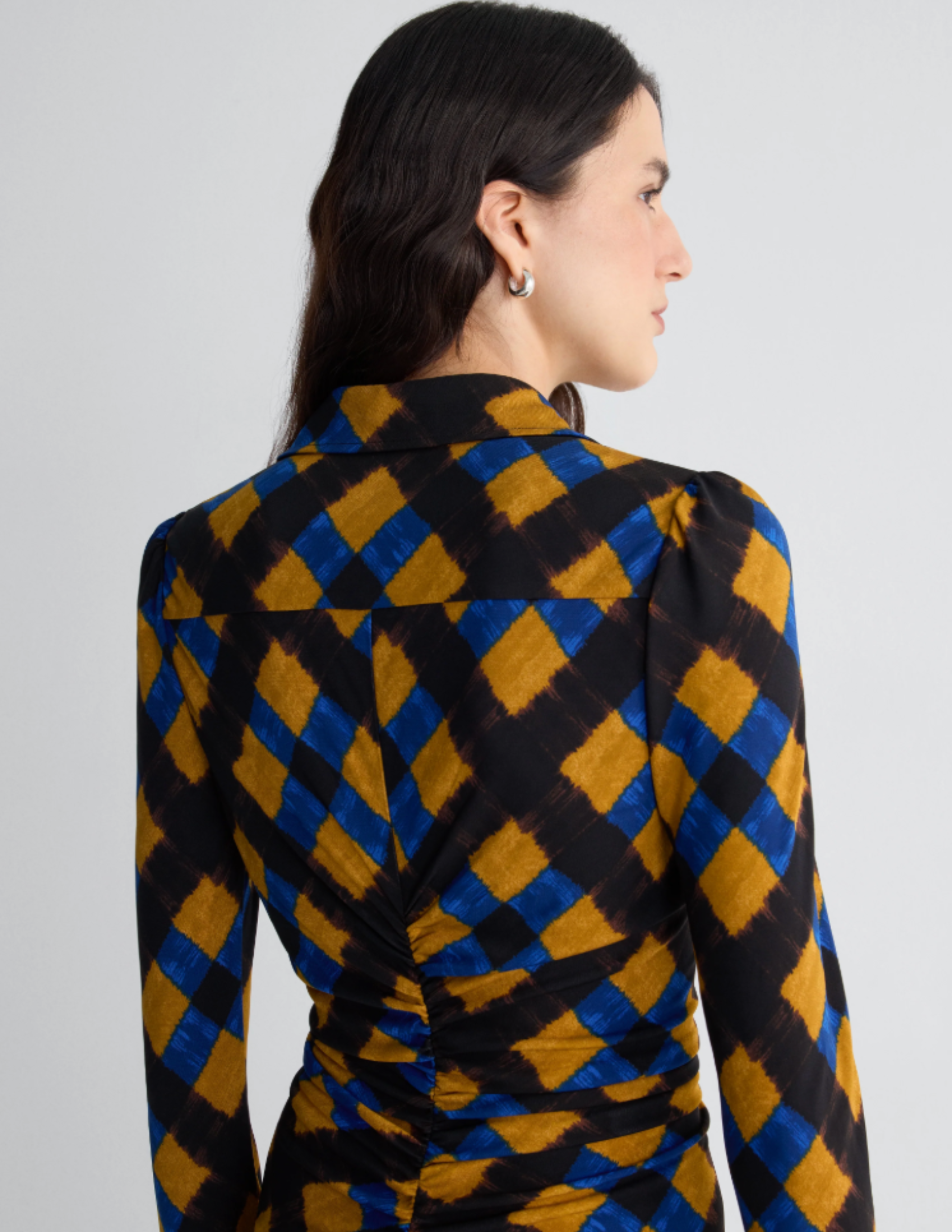 Model wearing a long-sleeve shirt dress in a blue, ochre, and black geometric print with front ruching and a button-front silhouette.