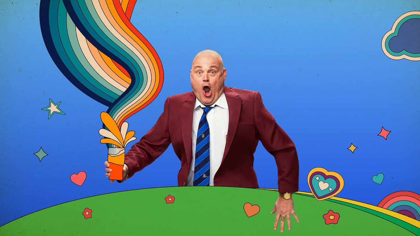 Al Murray in a burgundy blazer holding a cartoon rainbow spray can against a bright blue illustrated background with hearts, stars and rainbow graphics.