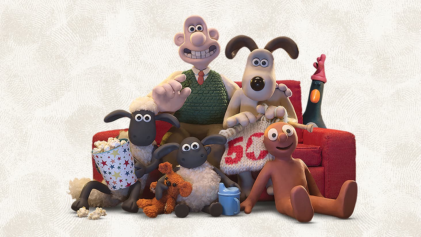 Promotional-style image featuring clay animation characters seated together on a red sofa against a light, textured background. At the centre sits a human character wearing a green knitted vest and tie, with an arm resting around a dog with long ears. Surrounding the central figures are several familiar characters: two sheep sitting on the floor in front, one holding or sitting beside a large tub of popcorn with some spilled on the floor; a small orange plush toy and a blue cup placed nearby; and another character reclining on the floor at the right. A tall bird character stands behind the sofa on the right side. The group is arranged closely together, facing forward, with a cosy, family-viewing atmosphere suggested by the sofa, snacks, and relaxed poses.