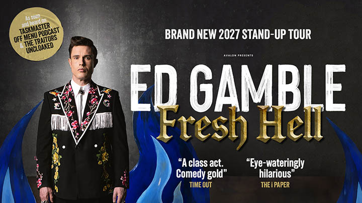 Promotional stand-up comedy poster with a person standing on the left wearing a black suit jacket decorated with colorful embroidered flowers and fringe details, against a textured grey background. Large white and gold text on the right reads “ED GAMBLE – FRESH HELL,” with smaller text above stating “Brand New 2027 Stand-Up Tour.” Additional quotes and review snippets appear alongside stylised blue flames rising from the bottom.