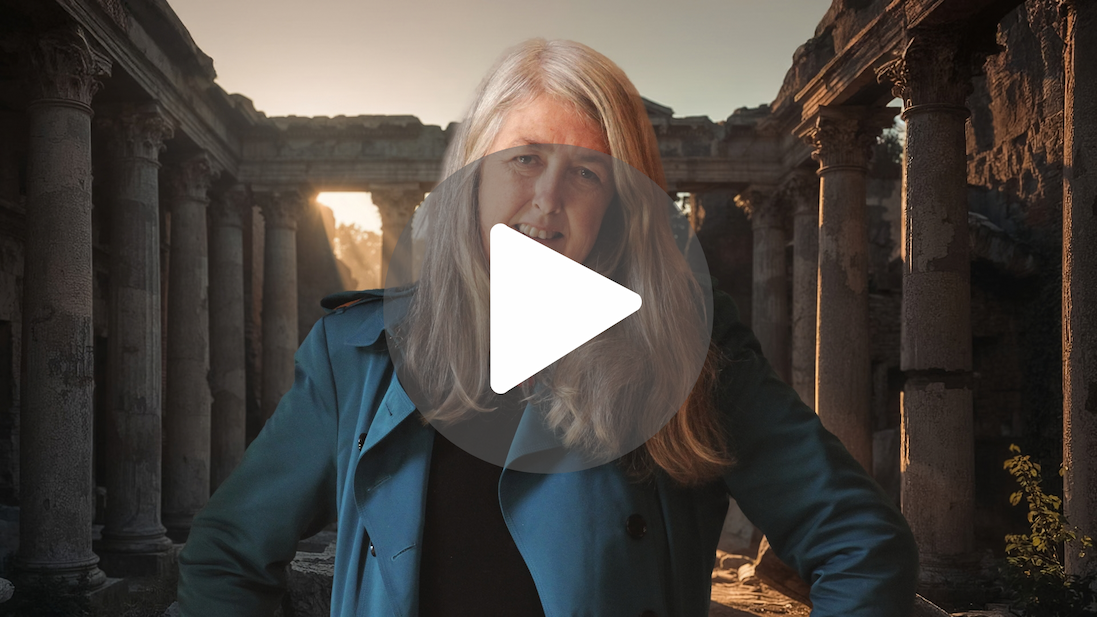 Promotional portrait of an author standing before ancient stone ruins and columns, with warm sunlight illuminating a historic archaeological setting.