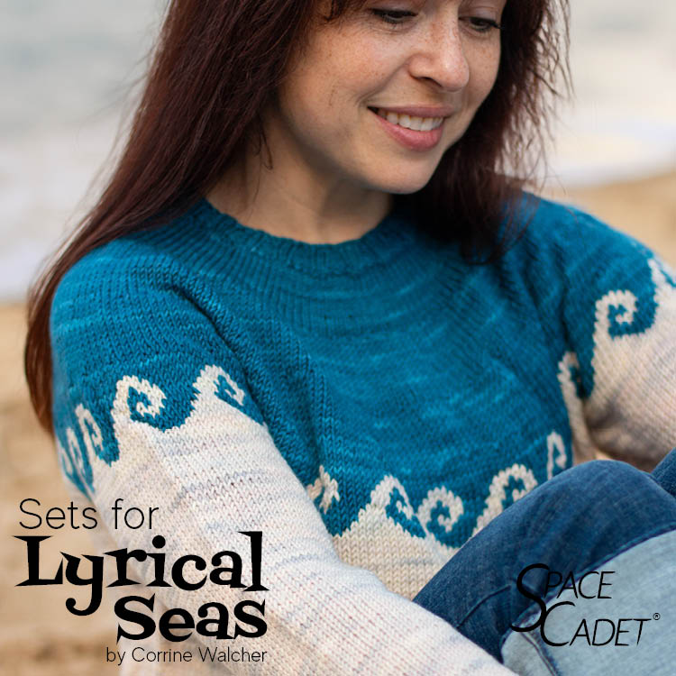 The Lyrical Seas Yarn Sets from SpaceCadet Yarn A model sits on the beach wearing the Lyrical Seas sweater by Corrine Walcher. The sweater is a yoked design with a wave motif in Sandbank pink-grey and Hello Sailor navy blue.