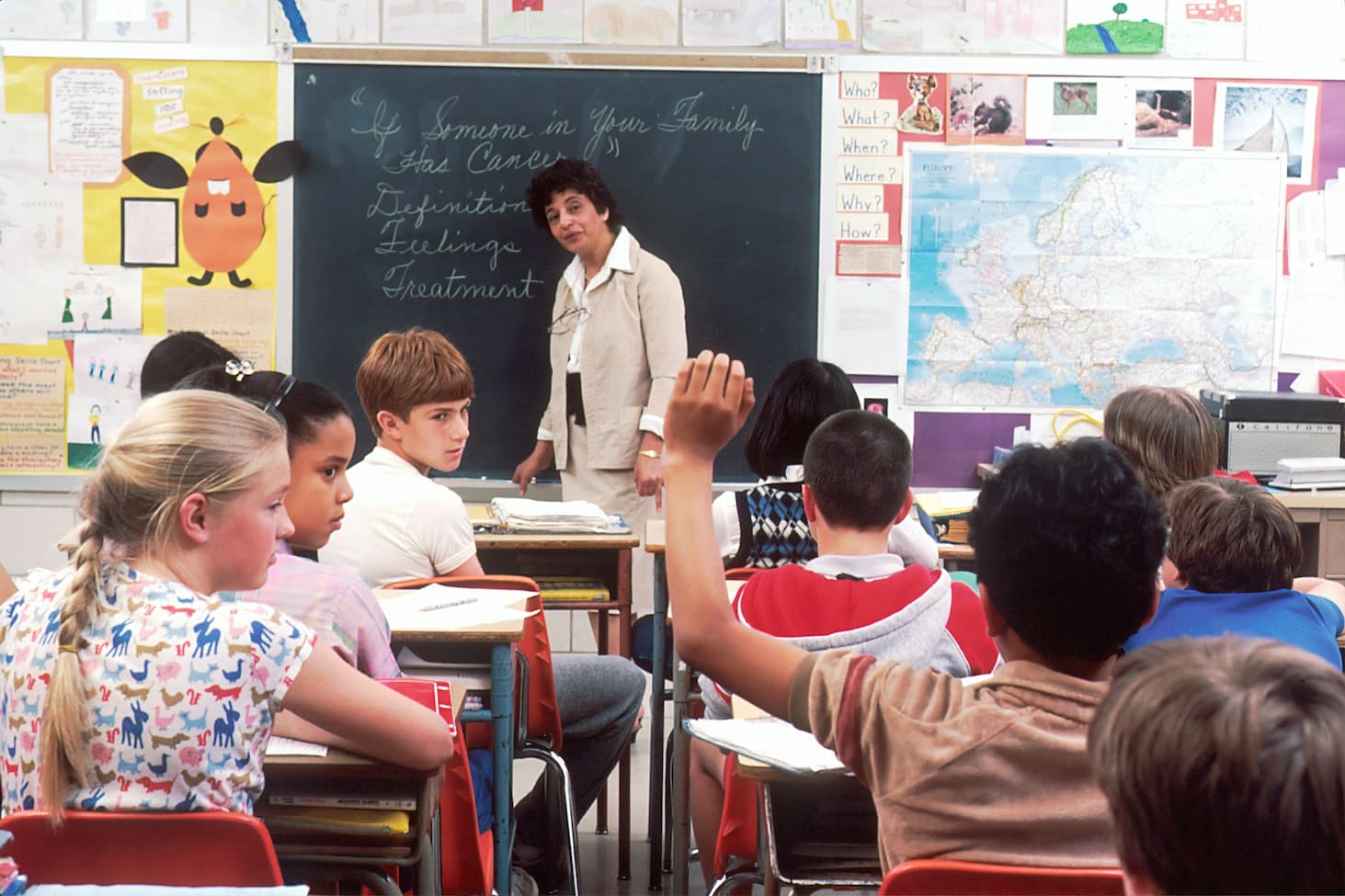 Unsplash image from National Cancer Institute photographer, Michael Anderson. Image shows children in classroom with teacher at front teaching