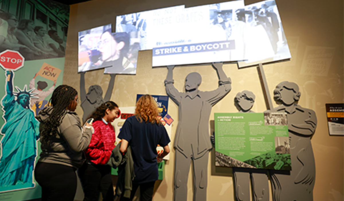 Three visitors viewing a museum exhibit on civil rights and protests featuring silhouettes holding signs.