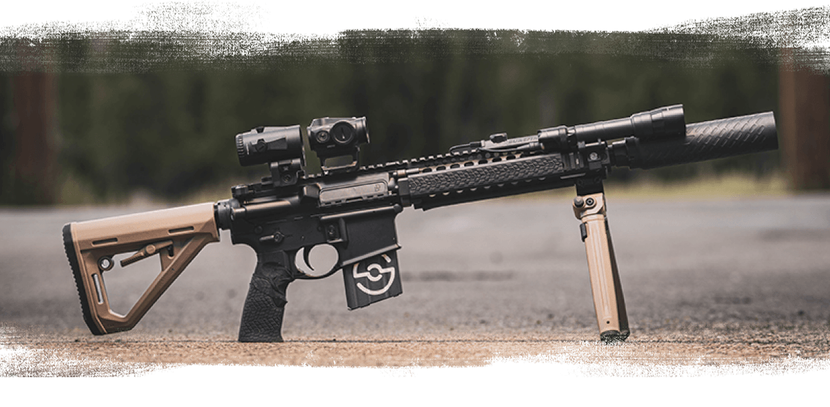 Modern rifle with optic, foregrip, and suppressor outdoors.