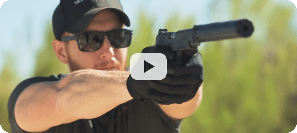 Person with handgun and suppressor outdoors.