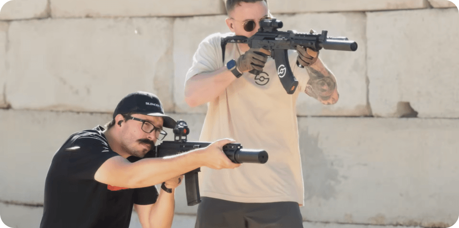 Two people aiming firearms with suppressors at range.