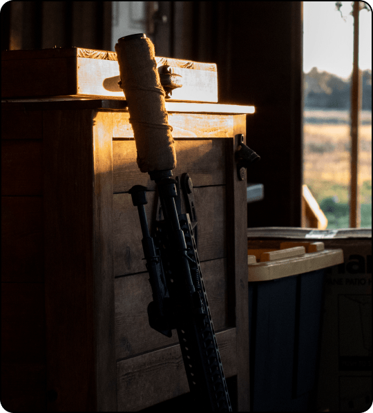 Rifle with wrapped barrel positioned against cabinet in storage area.