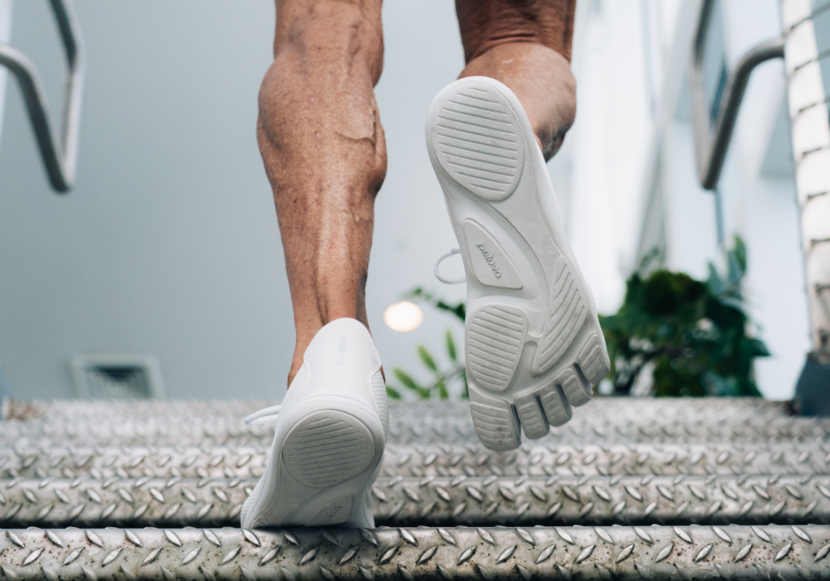 Close-up of legs mid-stride, sole of five-toe shoe flexing upward off the ground.