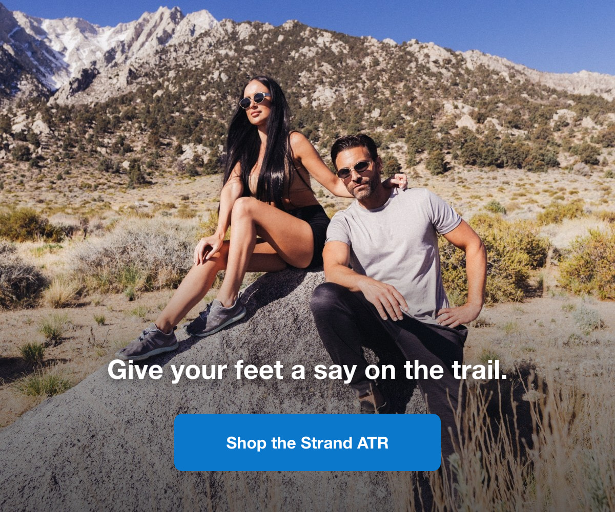 Couple sitting on rocks overlooking mountain trail scenery. Shop the Strand ATR.