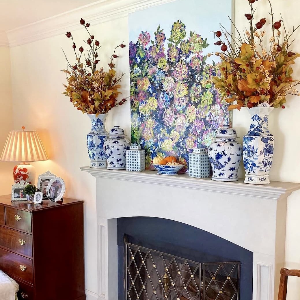 Fireplace mantel styled with seasonal décor – Blue and white vases, festive artwork, and seasonal stems for a home refresh.
