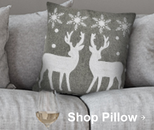 Gray holiday pillow with white reindeer and snowflake design on a light gray sofa.