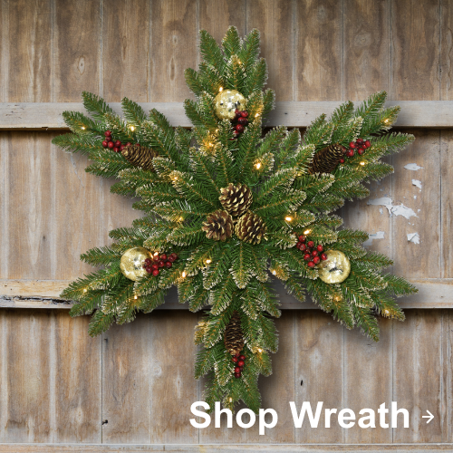 Star-shaped Christmas wreath with pinecones, red berries, gold ornaments, and lights on a wooden wall.