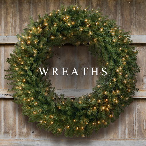 Large green Christmas wreath with warm white lights hanging on a wooden wall.
