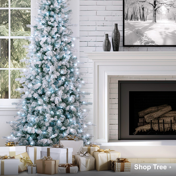 Flocked Christmas tree with white lights beside a fireplace, surrounded by gold and white wrapped presents.