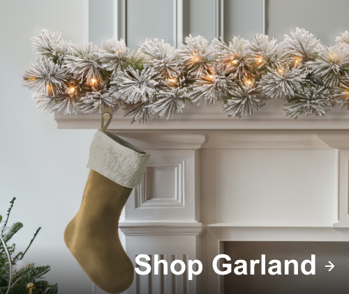 Snow-frosted garland with lights and a gold stocking hanging on a white fireplace mantel.